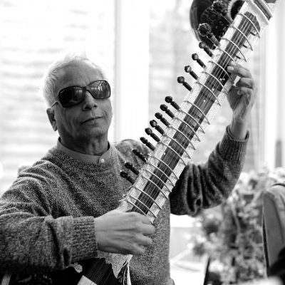 black and white photo of Baluji sitting on a chair with his sitar in hand.