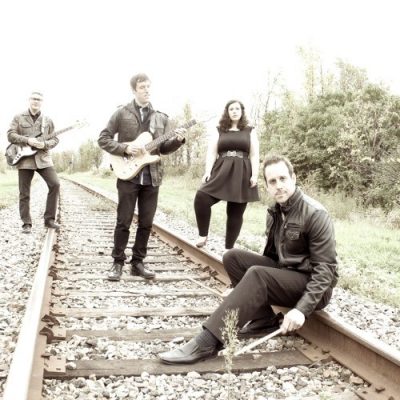 A black and white photo of the 4 members of Lucas Haneman Express , well dressed, standing on a train track.