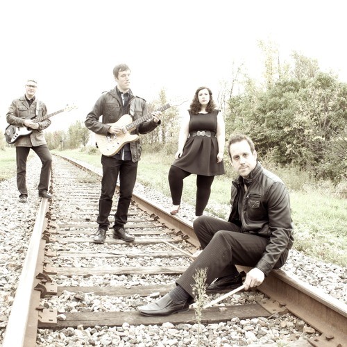 A black and white photo of the 4 members of Lucas Haneman Express , well dressed, standing on a train track.