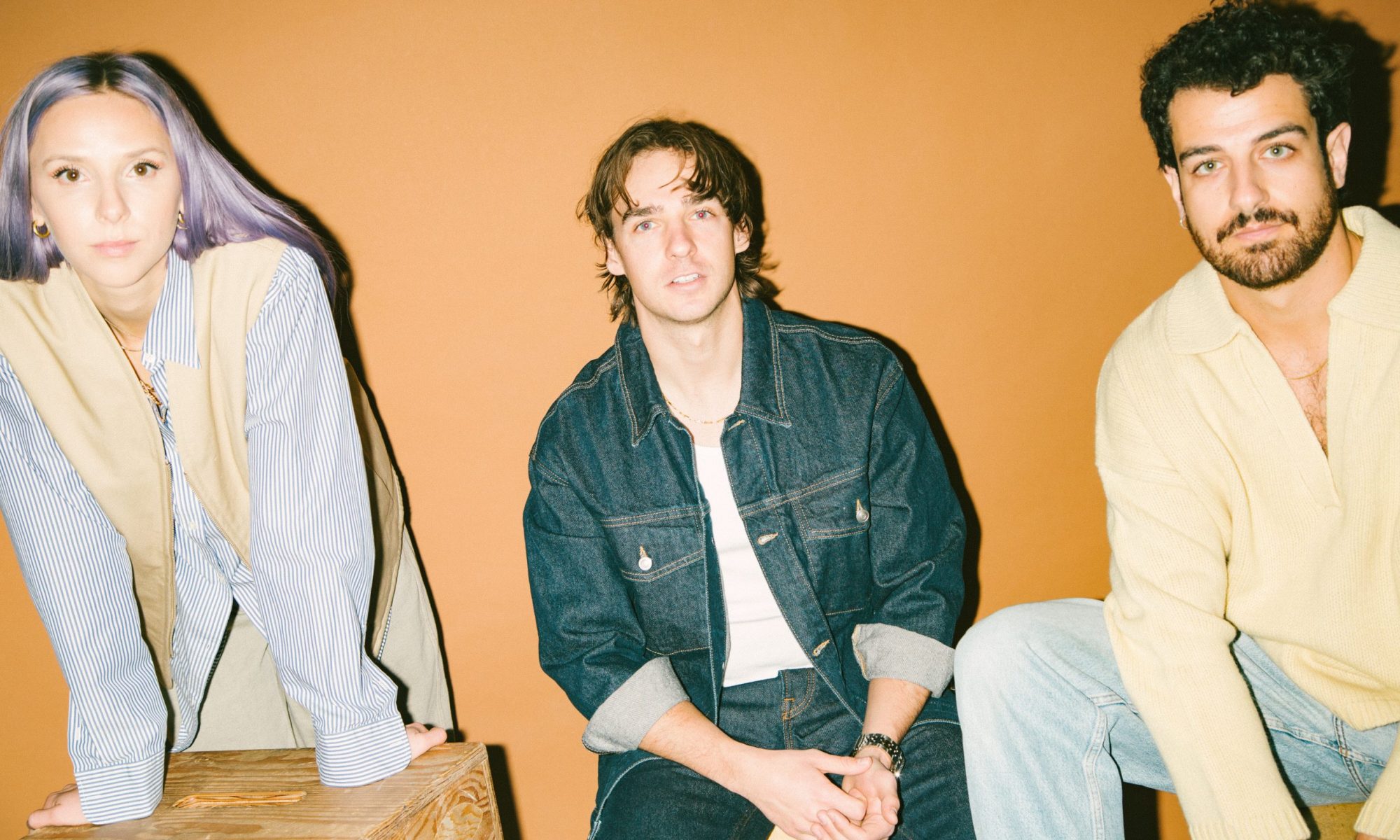 A photo of the three members of Wild Rivers against a gold background wall