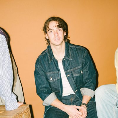 A photo of the three members of Wild Rivers against a gold background wall