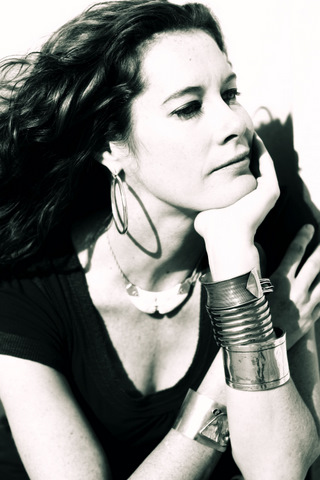black-and-white Photo of Caitlin Smith sitting on a chair, wearing a black sleeveless dress with long, black hair, with her chin resting on her left hand propped up on her elbow.