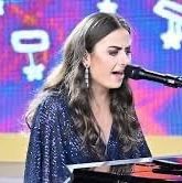 Lara pictured on the Carols By Candlelight stage last year on Christmas eve seated at a grand piano wearing a beautiful sparkly dark blue dress, singing and playing the piano.